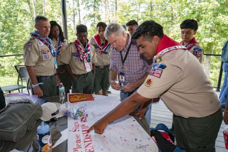 Trevor Rees-Jones, center, and a Scout from his local council (Circle Ten Council) look for the perfect spot to sign a friendship pledge on the deck of The Rees-Jones Foundation Leadership Veranda during the 2019 World Scout Jamboree.