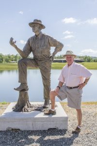 John Tickle poses with his bronze likeness along the banks of Tickle Lake.
