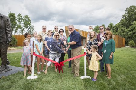 Craig Fenneman, center, cuts the ribbon to dedicate a bronze statue in his honor alongside his wife, Mary, and his family.